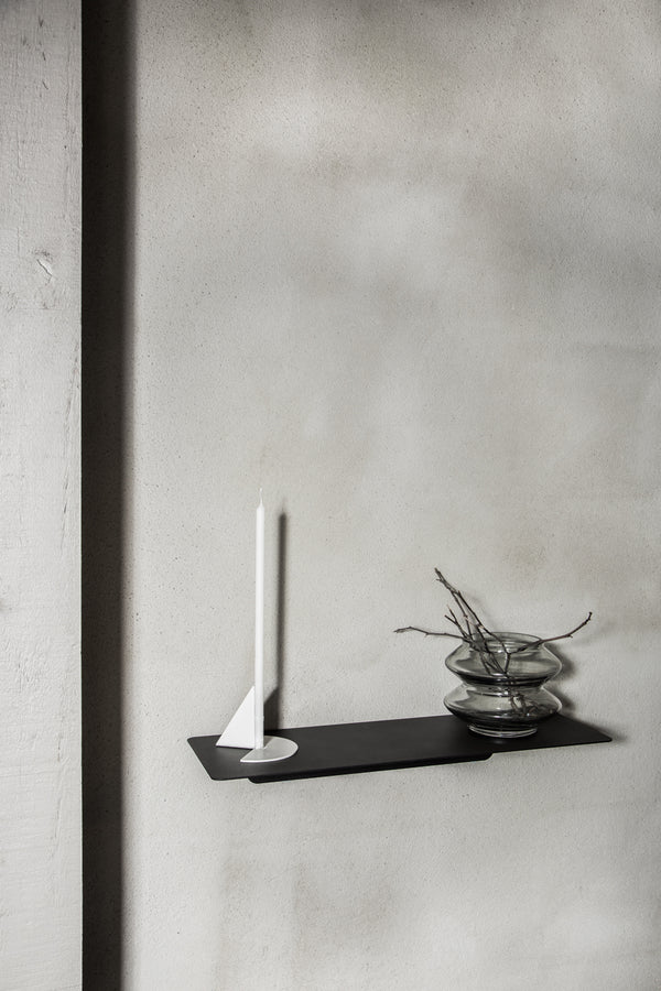 A functional black shelf, Made of Tomorrow FOLD Ledge 450mm ∙ White, featuring a candle placed on it.