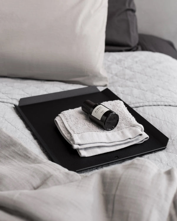 A FOLD Tray ∙ Black (Large) on top of a bed with a towel on it.
