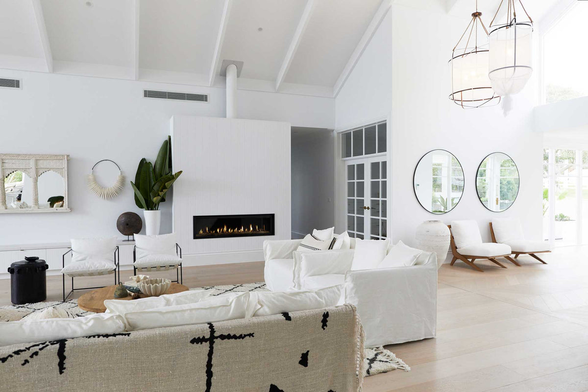 White living room with a fireplace, sofas and a round mirror