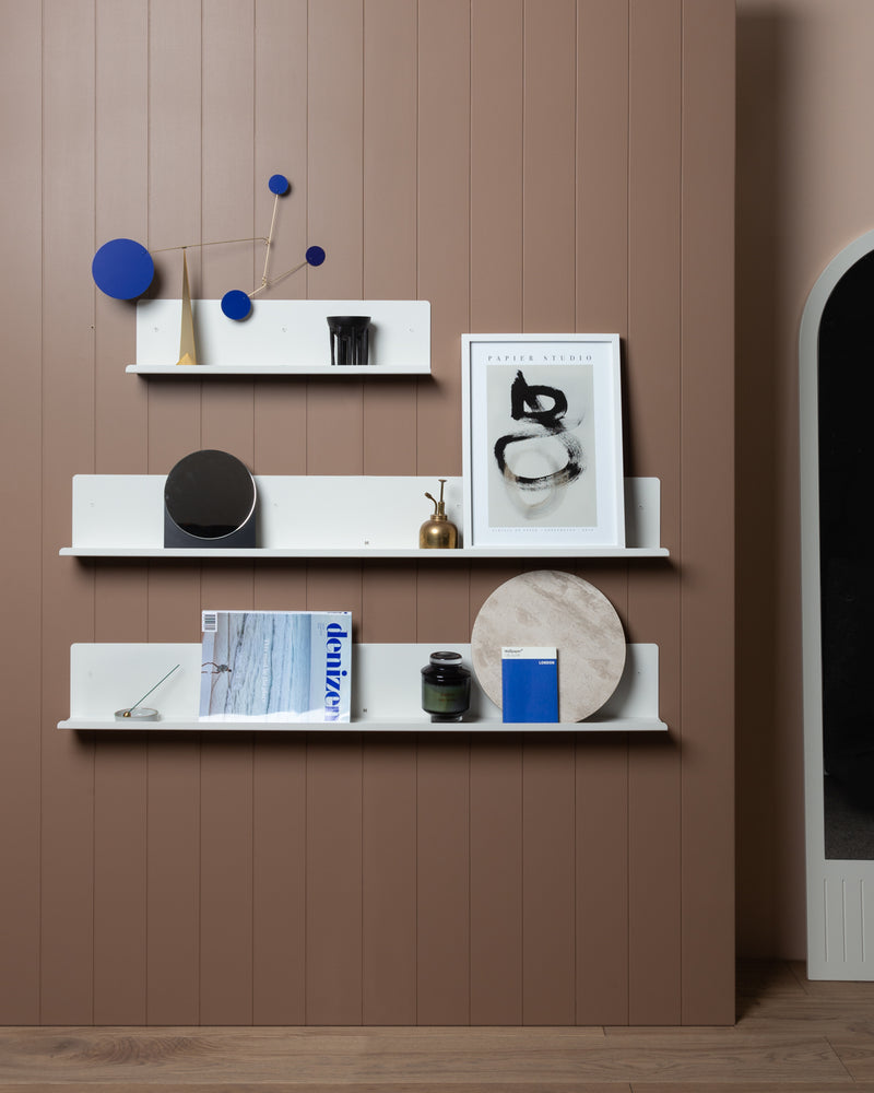 A wall shelf with display space designed with FOLD Display Ledge 600mm ∙ White by Made of Tomorrow on a brown wall.