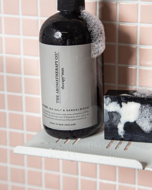 A FOLD Shower Shelf ∙ White sits on a shower shelf next to a soap dispenser.