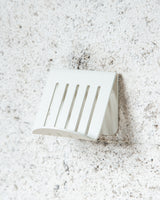 A FOLD Soap Block Holder ∙ White shelf hanging on a concrete wall, made by Made of Tomorrow.