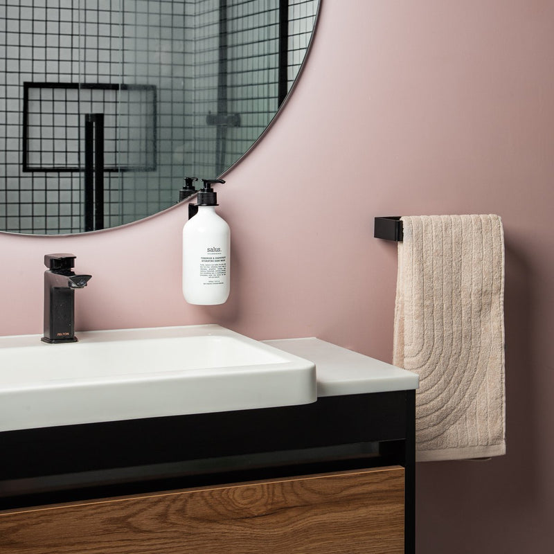 A bathroom with pink walls and a black sink. The Made of Tomorrow FOLD Bottle Holder ∙ Black adds a touch of functionality to this stylish space, seamlessly blending into the overall design.