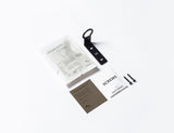 A compact package consisting of a FOLD Bottle Holder ∙ Black from Made of Tomorrow and other essential items for both bathroom and office use.