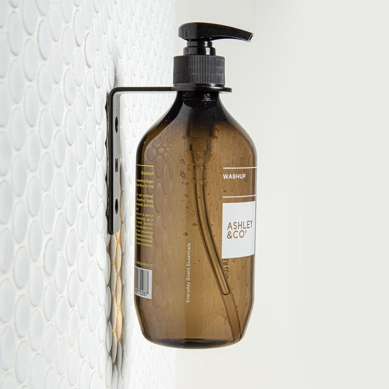 A Made of Tomorrow FOLD Bottle Holder displaying a bottle of soap in a bathroom or office setting, hanging on a wall.