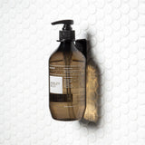 A Made of Tomorrow FOLD Bottle Holder ∙ Black securely hangs a bottle of soap on a bathroom or office wall.