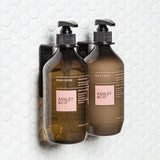 Two FOLD Bottle Holder ∙ Black from Made of Tomorrow, one in a bathroom and the other in an office, are hanging on a wall.