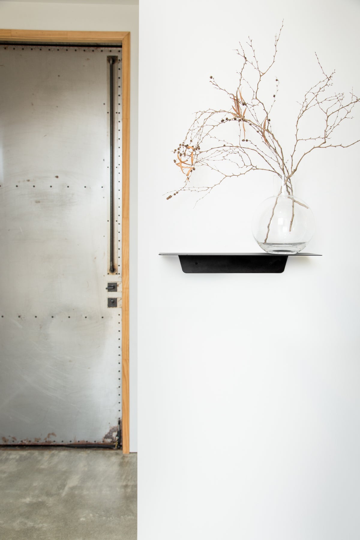 A FOLD Ledge 450mm ∙ Black vase made by Made of Tomorrow on a functional shelf next to a door.