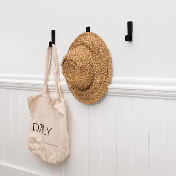 A Fold Loop Hook - White made by Made of Tomorrow hangs on a hook next to a tote bag.