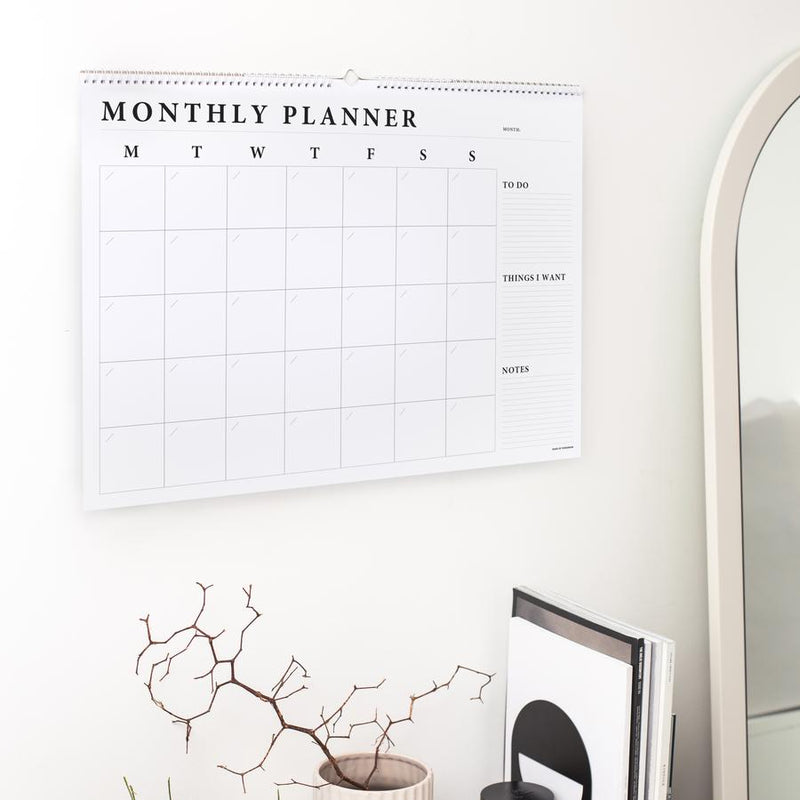 A desk with a Monthly Wall Planner hanging on the wall by Made of Tomorrow.
