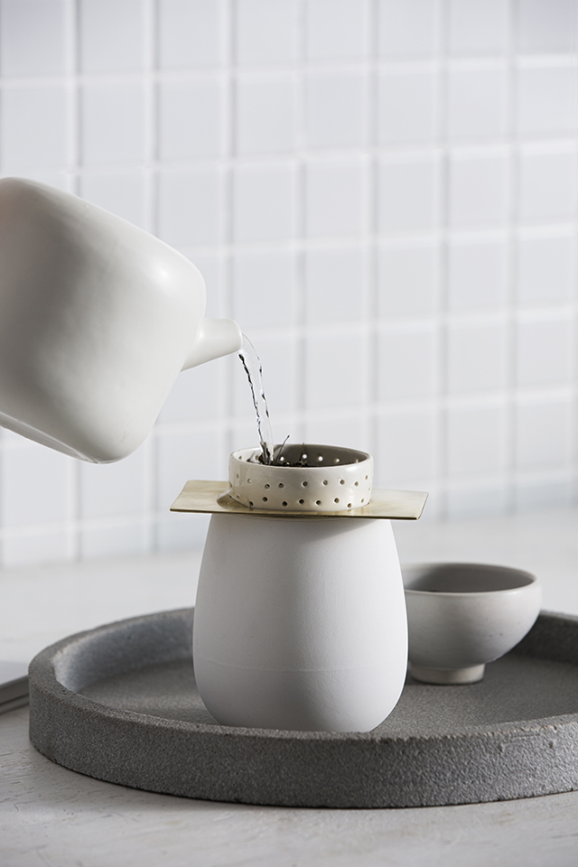 A Zakkia Two Piece Coffee Brewer with a sleek white design is being delicately poured onto a brass plate, creating a visually appealing coffee brewing experience.