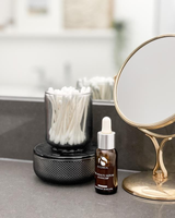 A bottle of ALLIRA ORGANIZER - SMOKE by Umbra sits next to a mirror on a bathroom counter, creating a serene and relaxing atmosphere.