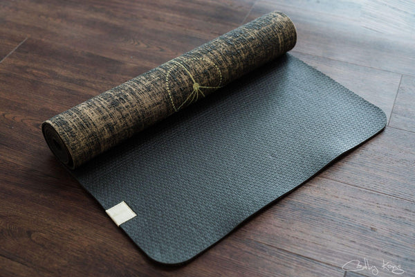 A Yogatribe | Organic Jute 100% Eco Yoga Mat - Various Options on a wooden floor.