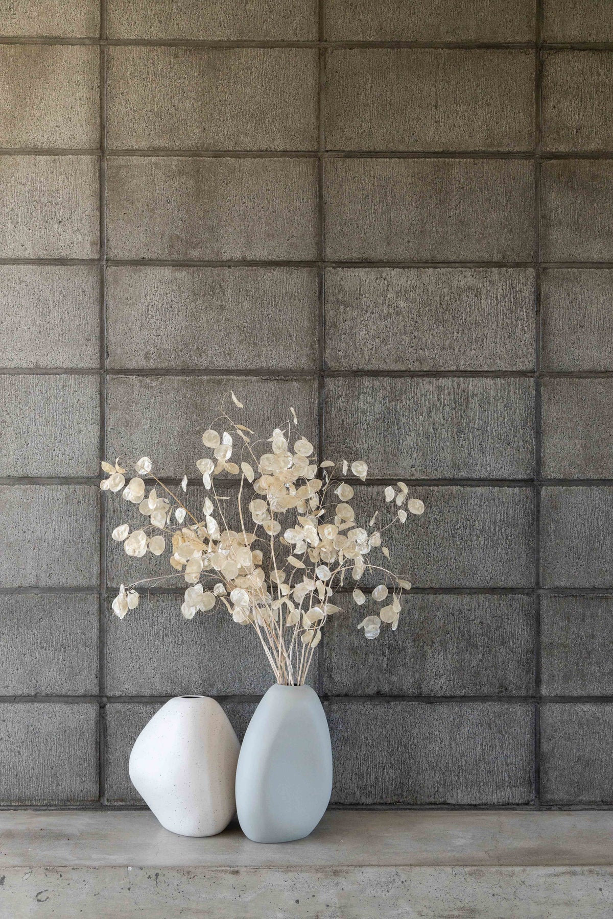 Two white Ned Collections Harmie vases sit on top of a concrete wall.