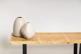 Two HARMIE Pebble Vases - Natural, hand-crafted by Vietnamese artisans, sit on a wooden bench.