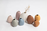Vietnamese artisans crafted a vibrant collection of Ned Collections' Harmie Vase - Seed Grey, featuring organic seed-like shapes, beautifully displayed on a pristine white surface.
