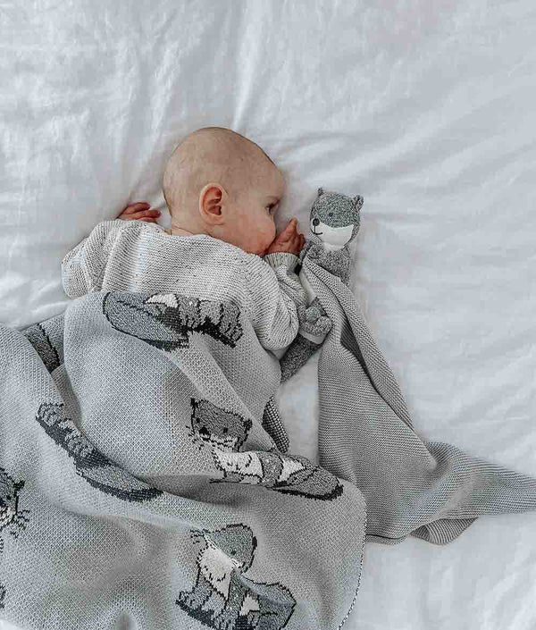 A baby is resting on a bed with a comfortable SEA OTTER SNUGGLY made by Bengali Collections, made of Oeko-tex Certified Cotton.
