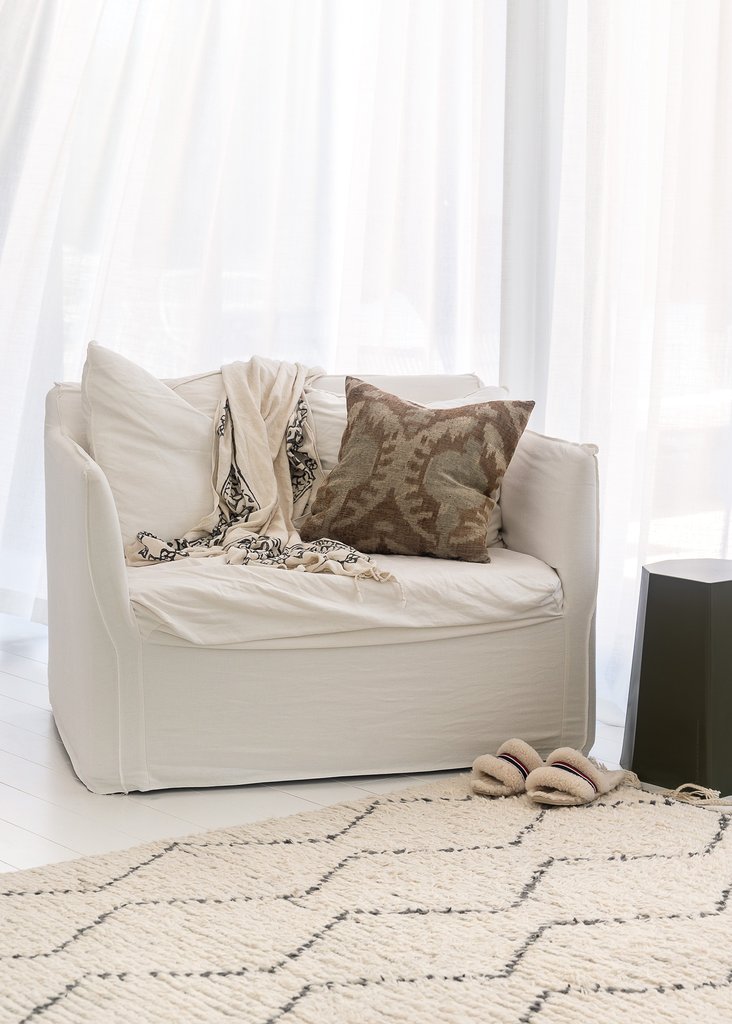 A white couch with a rug in front of Our Spaces - Contemporary New Zealand Interiors book.