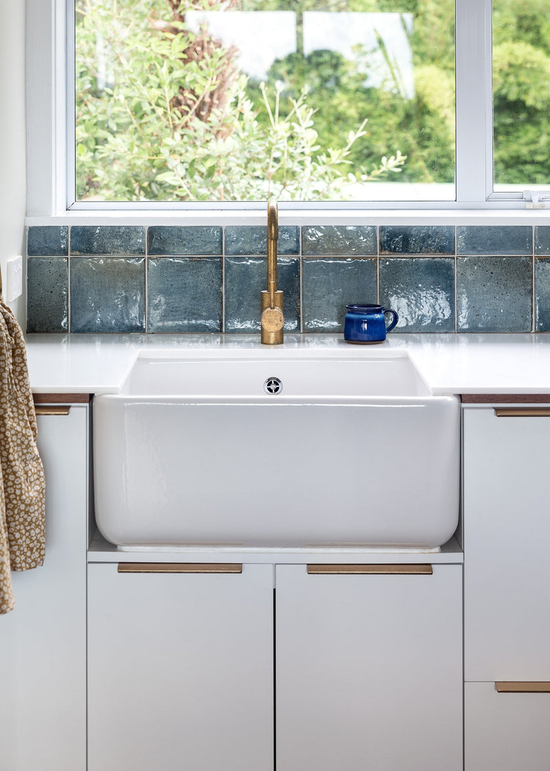 A white Our Spaces - Contemporary New Zealand Interiors sink in a kitchen with a window.