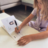 A Kiwi kid writing on a piece of paper, learning to speak TE REO MĀORI FOR PRESCHOOLERS by As We Are Illustration.