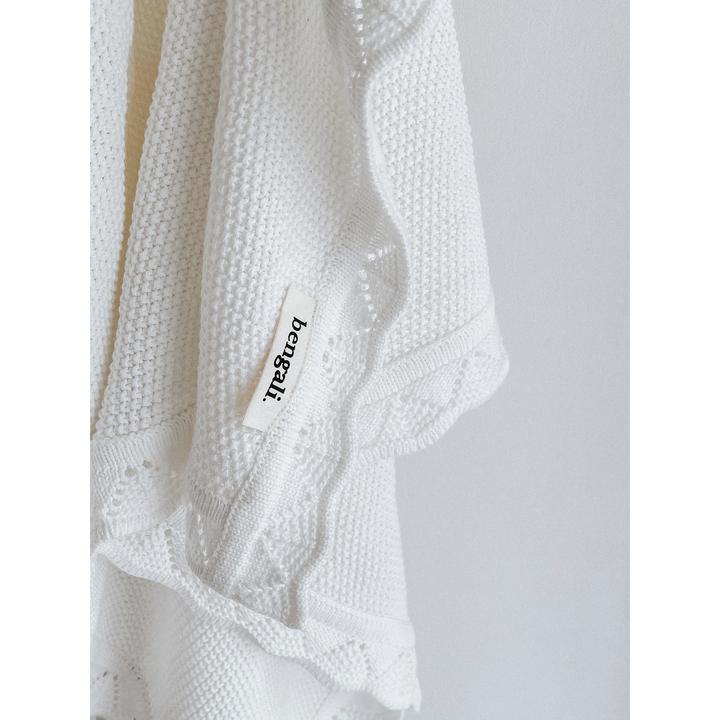 A White Heirloom Blanket, made of Oeko-tex® certified cotton, hanging on a hanger from Bengali Collections.
