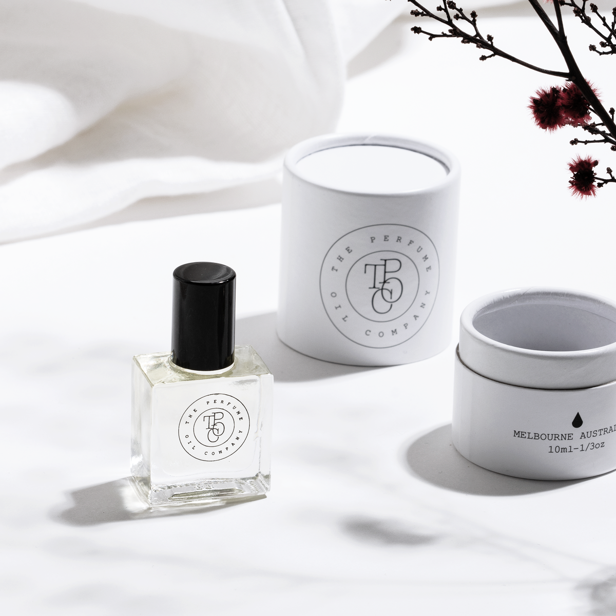 Perfume oil bottle with a gift tube and small tin beneath bare branches
