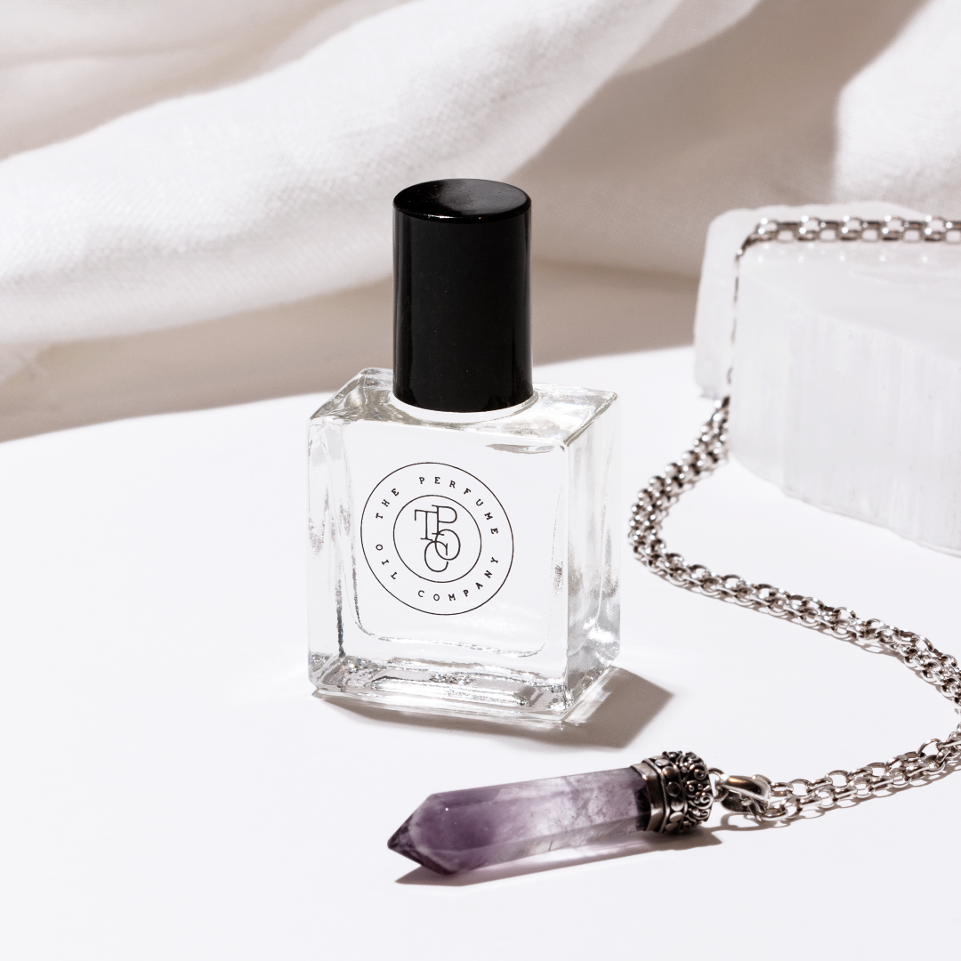 Perfume oil bottle beside a crystal pendant necklace on linen