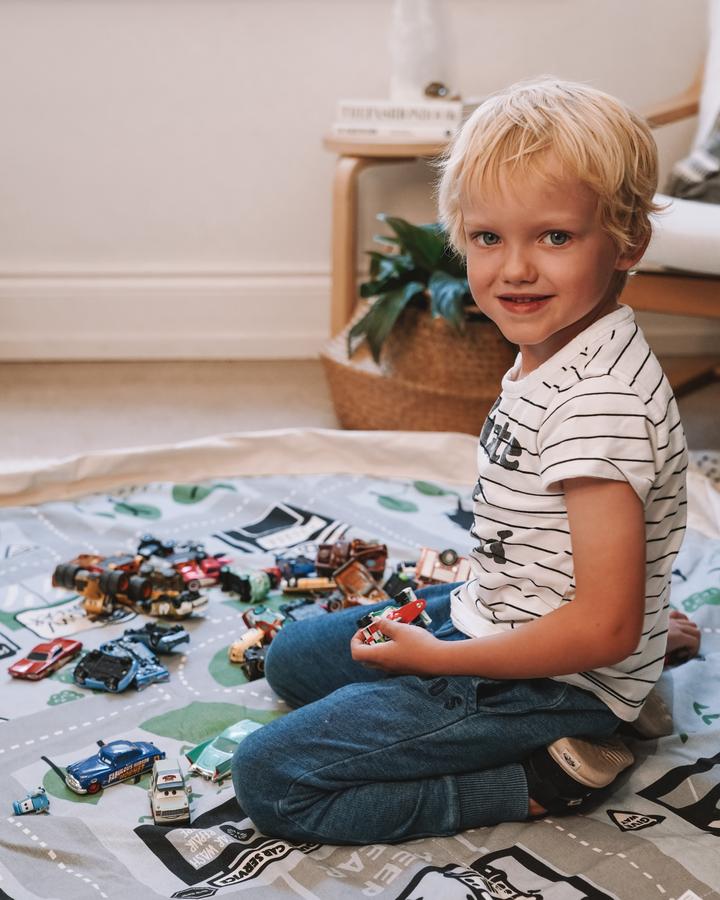 A young boy engaging in imaginative play on a Play Pouch with Wow Town Track Interactive toy cars.