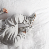 A baby is laying on a bed wearing LTL BIG | URBAN SLIP-ON IN MESSY SPOT shoes made of natural leather.