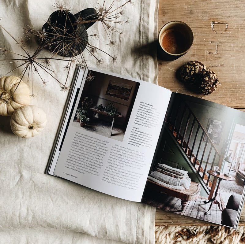 A "Calm | Interiors to Nurture, Relax and Restore | Sally Denning" magazine open on a table next to a cup of coffee in a calming home.