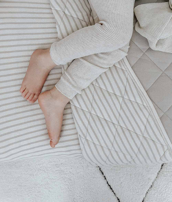 A child's feet laying on top of a bed with the REVERSIBLE QUILT - OATMEAL PINSTRIPE from Bengali Collections.