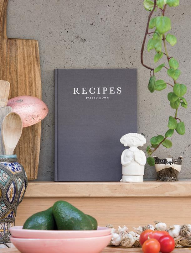 A Write To Me journal with Recipes Passed Down is sitting on a shelf next to a bowl of vegetables.