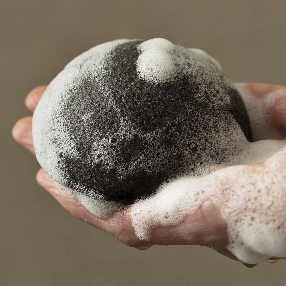 A person using a Florence Konjac Premium Facial Puff Sponge with Bamboo Charcoal deep cleans their pores.