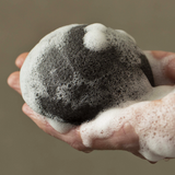 A person using a Florence Konjac Premium Facial Puff Sponge with Bamboo Charcoal deep cleans their pores.