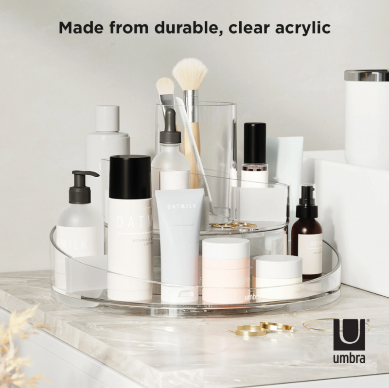 A Cascada Cosmetic Organizer by Umbra, a clear acrylic tray with cosmetics on it, featuring a rotating base.