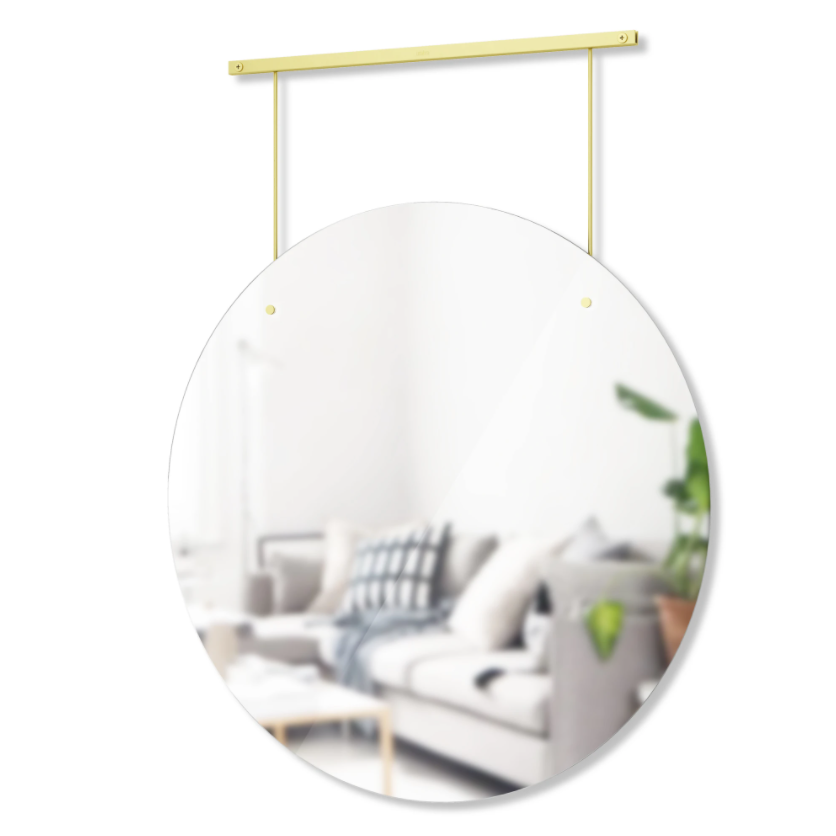 Umbra Exhibit round mirror suspended from its brass rail, reflecting a lounge