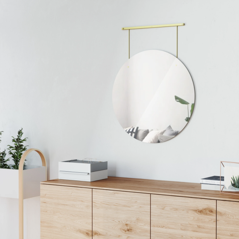 Umbra Exhibit round brass mirror above a timber sideboard in a white room
