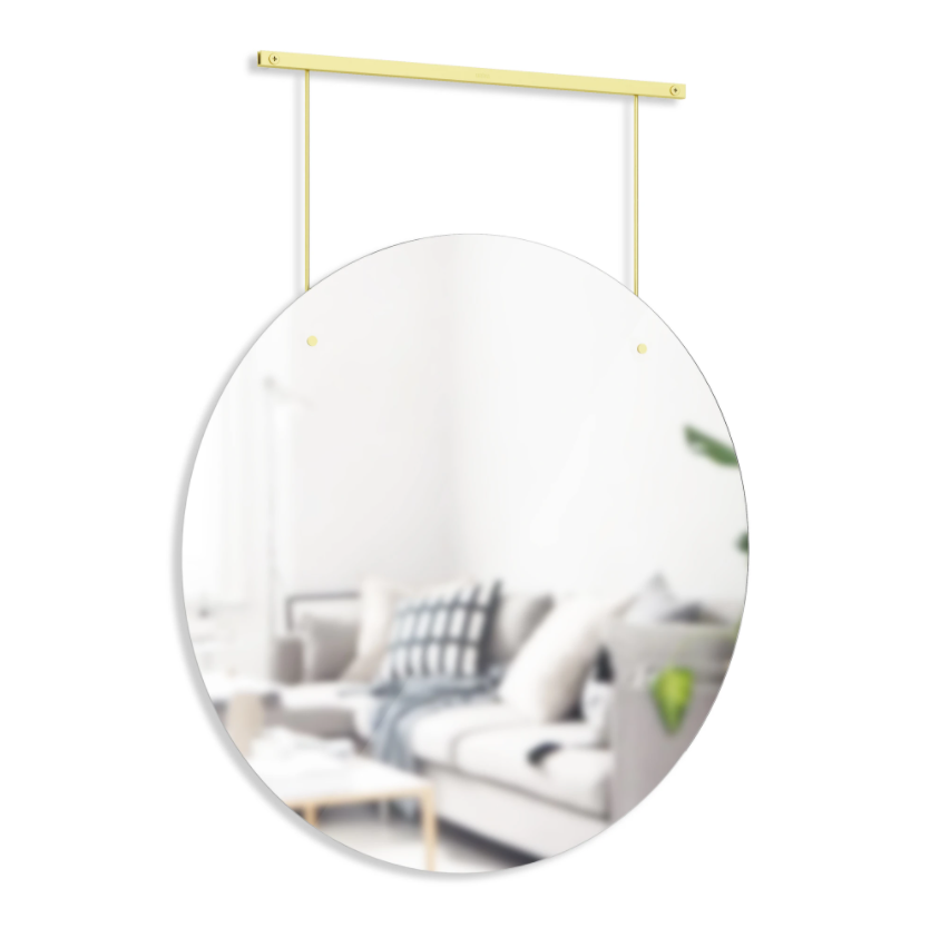 Umbra Exhibit round brass mirror hanging from its slim wall rail
