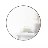 A decorative HUBBA MIRROR 34 TITANIUM from the Umbra range, sitting on top of a white table.