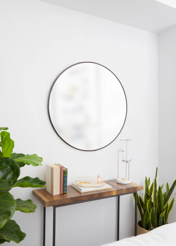 A white bedroom with an Umbra Hubba Mirror 34 Titanium and a plant on the table.