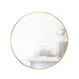 A decorative metal frame round gold Hubba Mirror 86cm Brass by Umbra, placed on a white table.