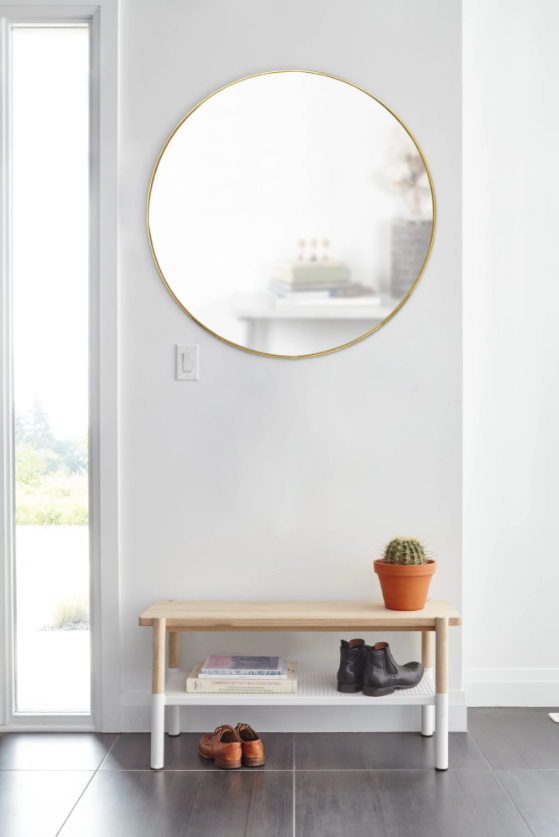 A Umbra HUBBA MIRROR 86cm BRASS with a decorative metal frame placed on a white bench in a white room.
