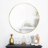 An Umbra HUBBA MIRROR 86cm BRASS framed mirror on a table next to a bottle of wine.