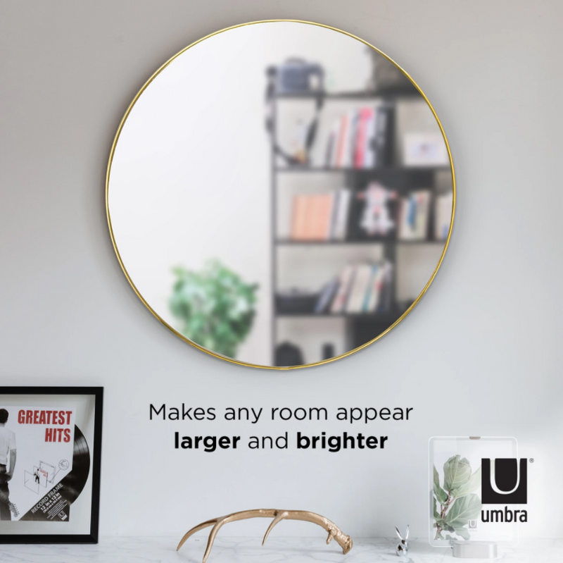 A decorative HUBBA MIRROR 86cm BRASS wall mirror with an Umbra book placed on a shelf.