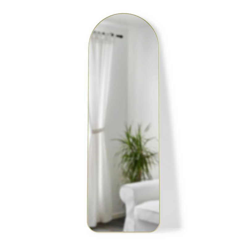 A Umbra HUBBA ARCHED LEANING MIRROR - BRASS in a room with a white couch and a plant.