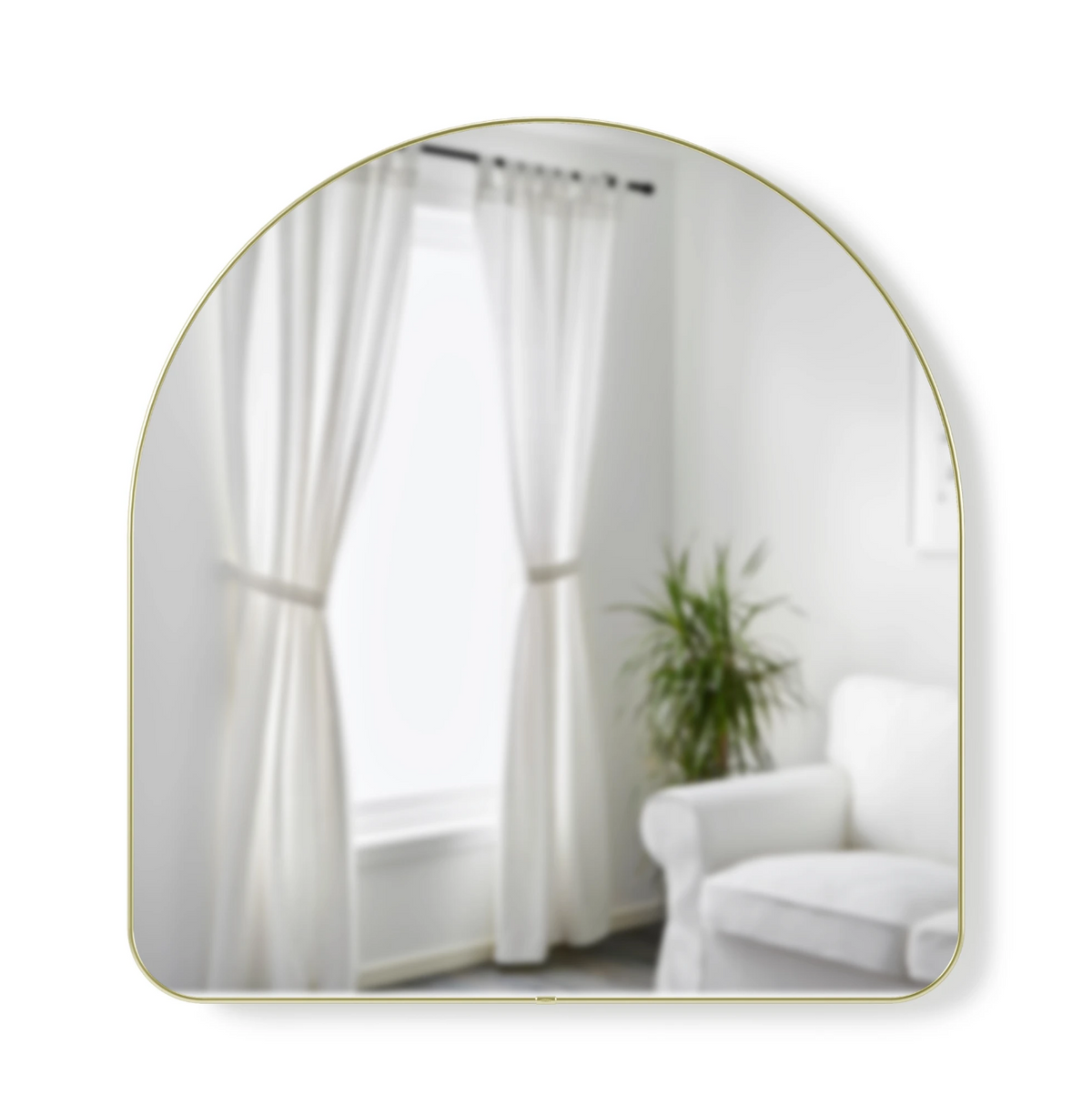 Umbra Hubba arched mirror in brass reflecting a curtained window and chair