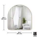A Umbra HUBBA ARCHED MIRROR - BRASS is shown in a decorative room with curtains.