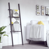 An Umbra Leana Ladder, a stylish storage solution, elegantly placed in a living room with a white couch.