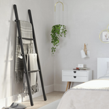 A black Umbra Leana Ladder, a versatile storage solution, in a bedroom with white walls and white bedding.
