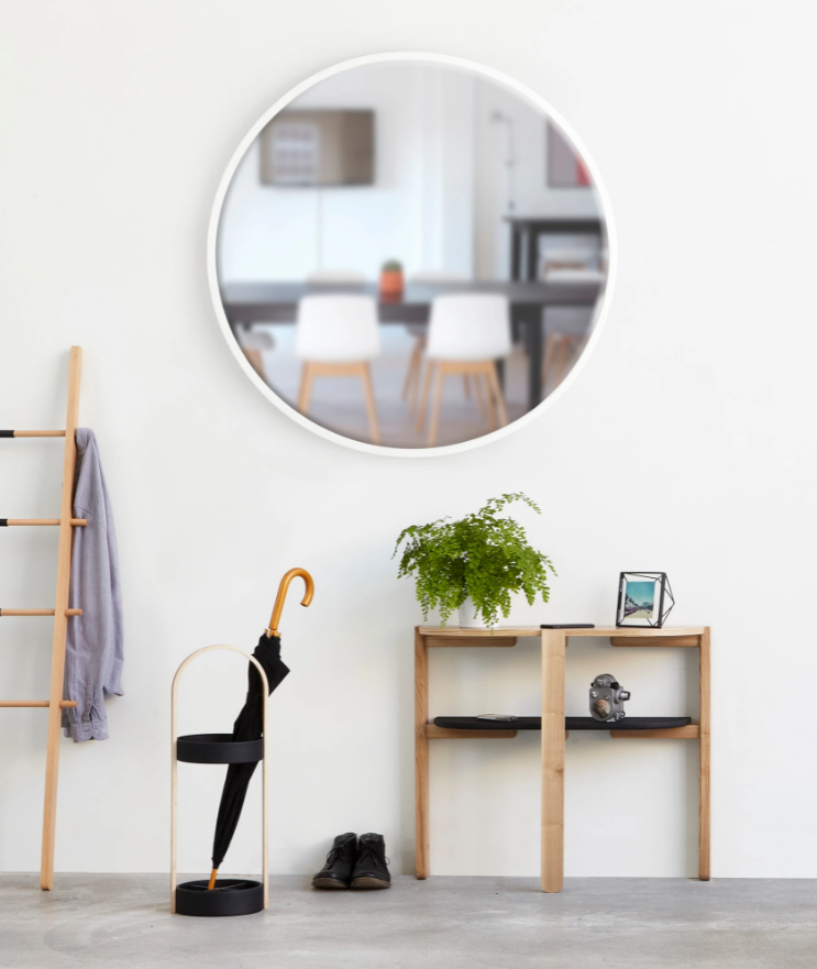 A durable HUB WALL MIRROR - White 94cm hangs on a wall next to an Umbra umbrella.